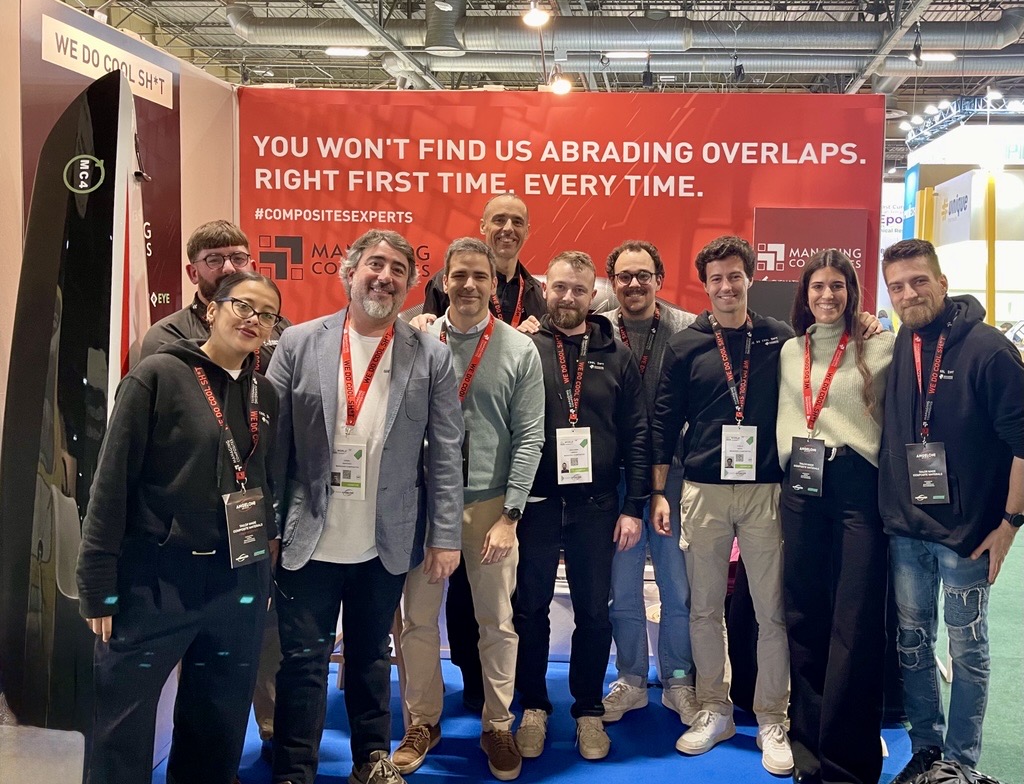 Ten members of the Managing Composites team pose at the company's booth at JEC World 2025 in Paris, next to the kayak