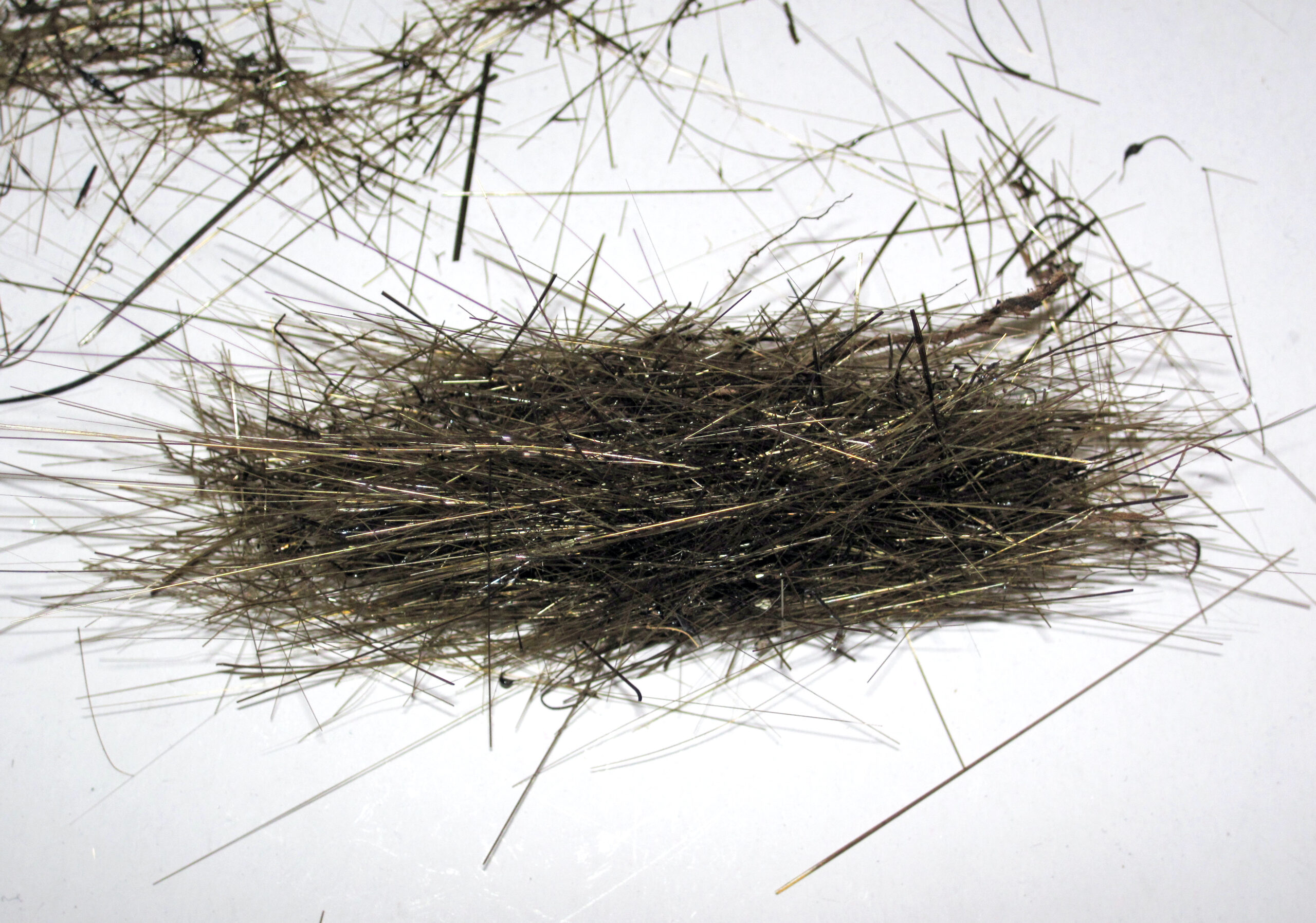 Processed basalt fiber in the form of loose fine filaments spread over a white surface