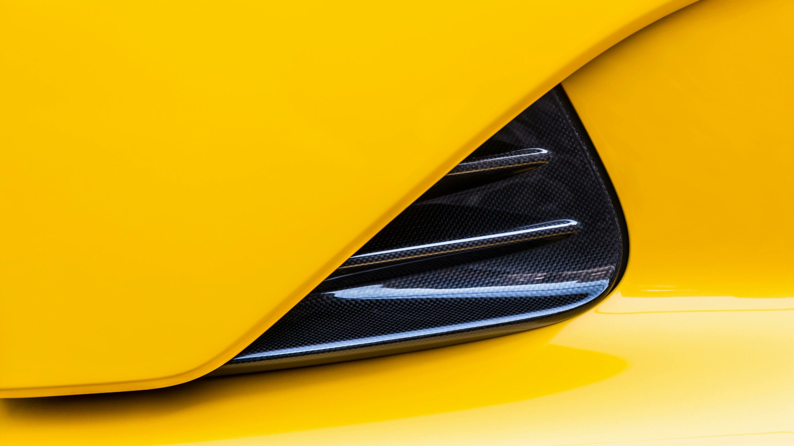 Carbon fiber detail on a yellow supercar – lightweight composite material for strength, aerodynamics, and high-performance design.