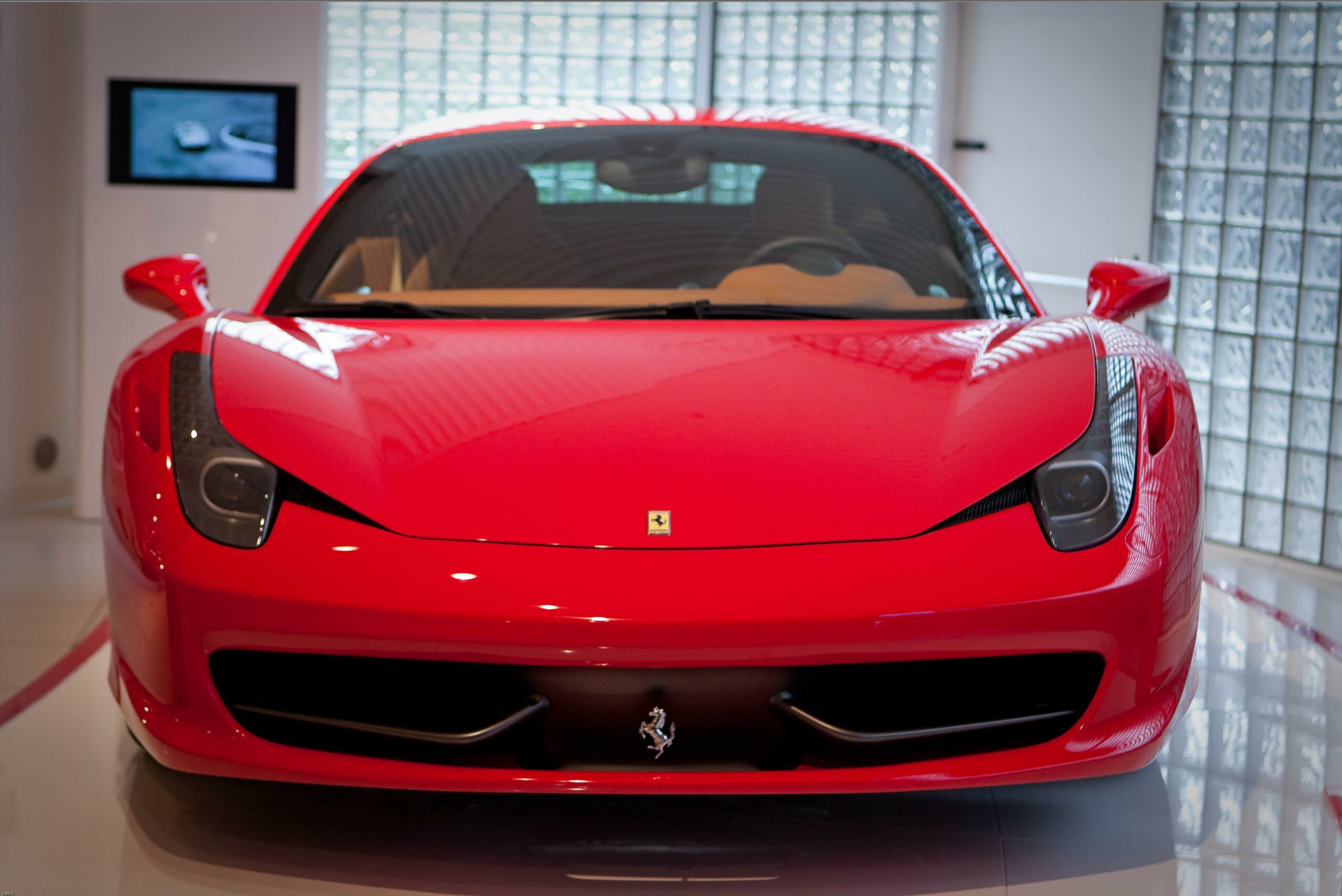 Front view of a red Ferrari 458 Italia sports car in a showroom, showing its aerodynamic body lines and signature Ferrari design.