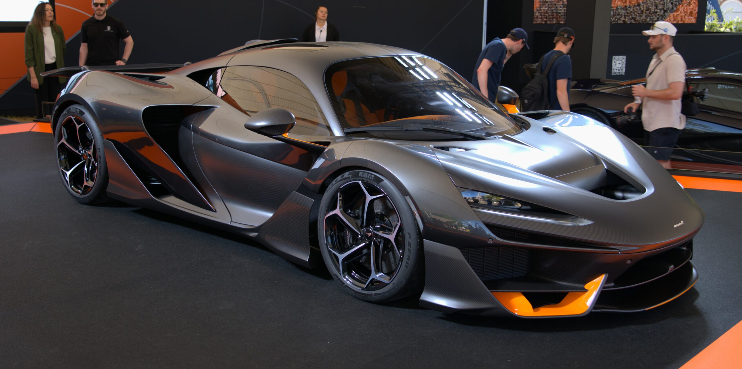 McLaren W1 hypercar on display, featuring sleek aerodynamic design, exposed carbon fiber bodywork, and orange accents around the front splitter.
