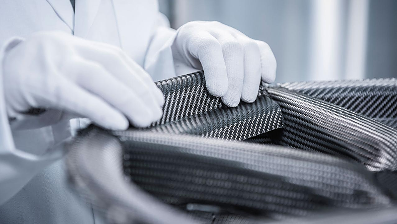 Close-up of a technician wearing white gloves handling carbon fiber during a composite manufacturing process