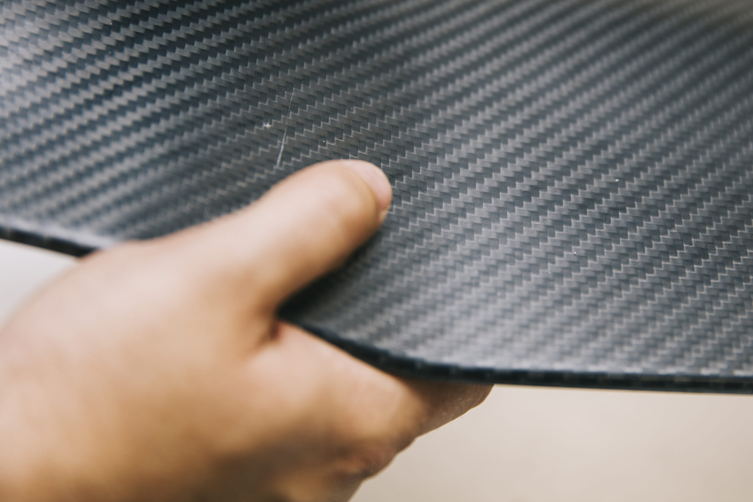 Hand holding a carbon fiber panel, showing its distinctive woven texture and lightweight composite structure.