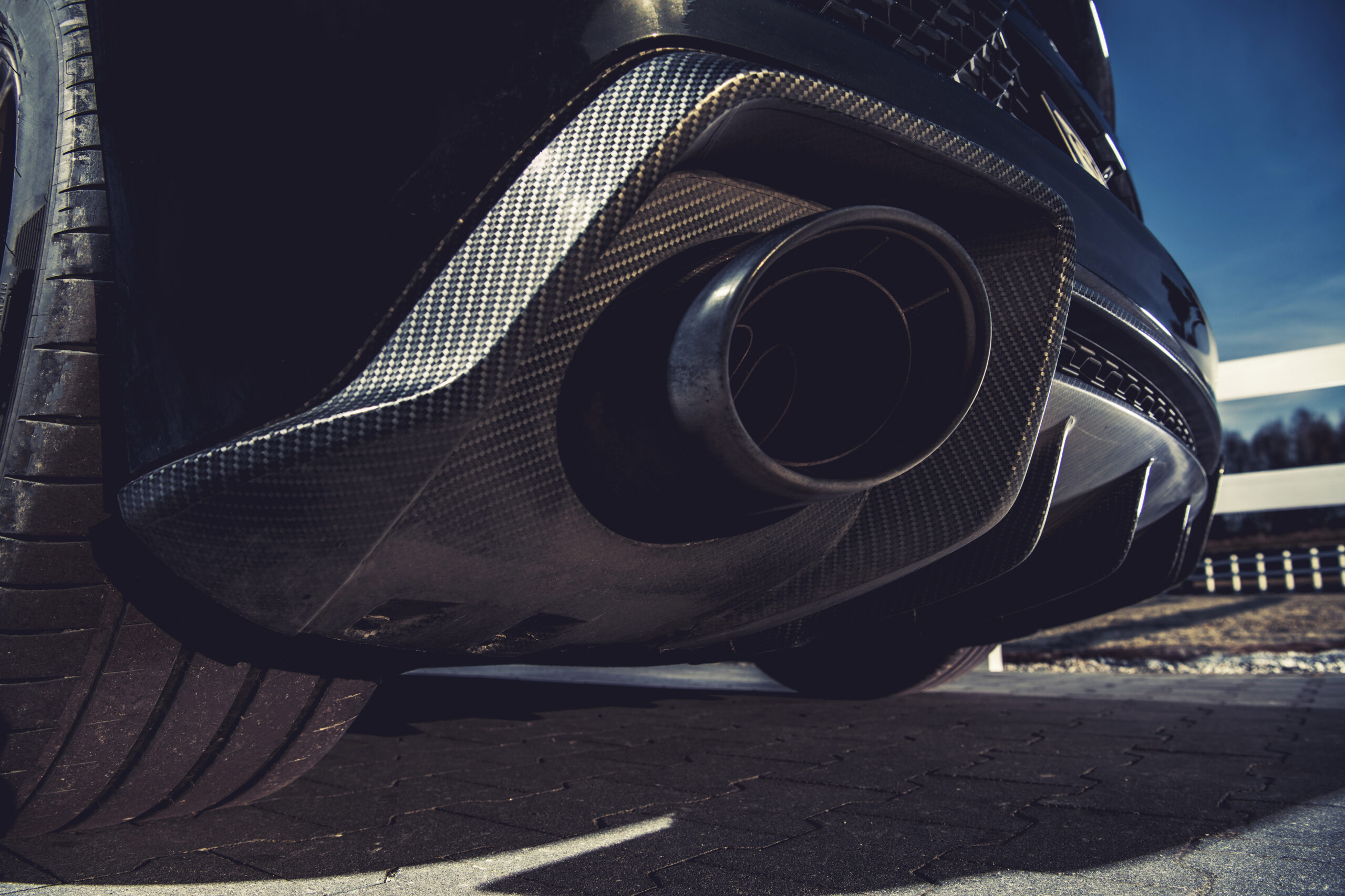 Close-up view of a sports car exhaust system and carbon fiber rear diffuser, highlighting composite material texture