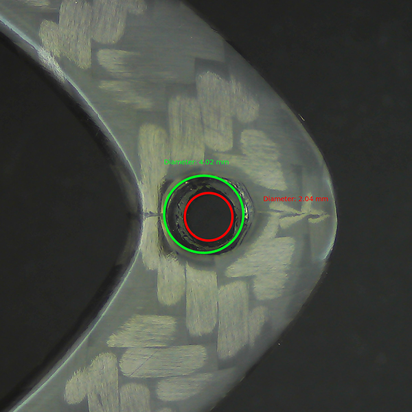 Computer-vision hole measurement on a carbon-fiber part showing detected inner and outer diameters with tolerance comparison.